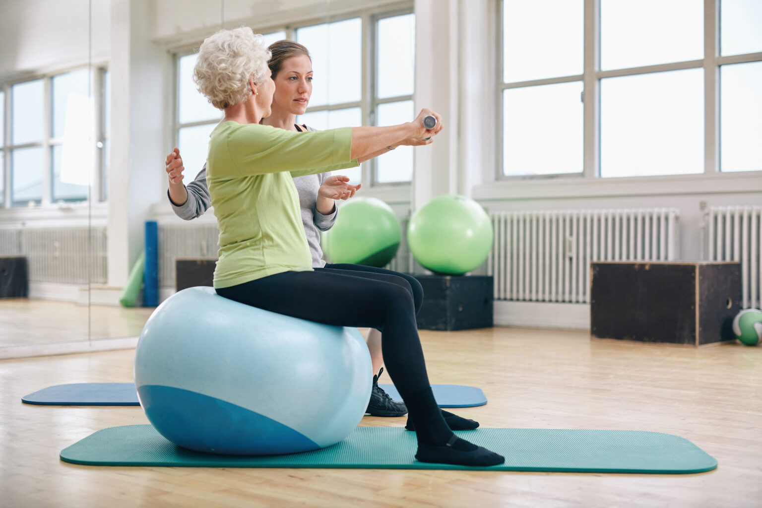 Das Bild zeigt eine ältere Frau, die unter Anleitung Übungen auf einem Sitzball durchführt.